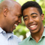 A supportive dad smiles and embraces his son who identifies as LGBTQIA.