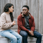 A young man and woman sit on stairs having a conversation about substance use treatment.